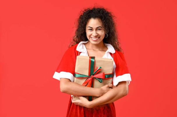 Młoda Afroamerykanka w stroju Mikołaja z pudełka na czerwonym tle - Zdjęcie, obraz