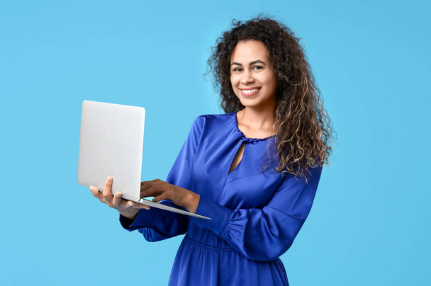 Jonge Afro-Amerikaanse vrouw met moderne laptop op blauwe achtergrond - Foto, afbeelding
