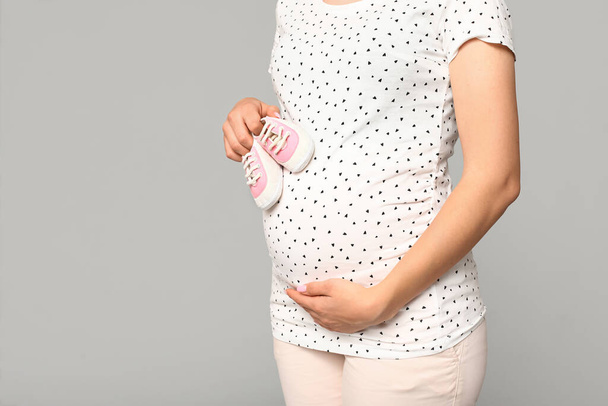 灰色の背景に赤ちゃんの靴を持つ美しい若い妊婦,クローズアップ - 写真・画像
