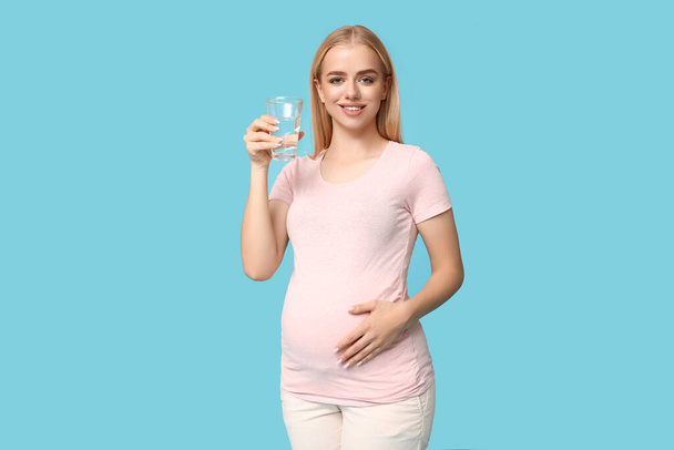 Piękna młoda kobieta w ciąży ze szklanką wody na niebieskim tle - Zdjęcie, obraz