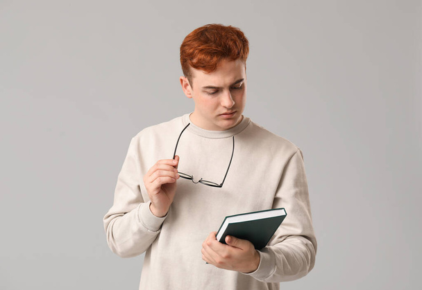 Young man with eyeglasses and book on grey background - Photo, Image