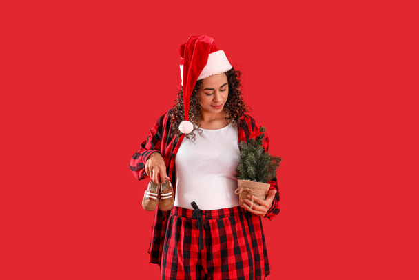 Donna afro-americana incinta a Babbo Natale con stivaletti e albero di Natale su sfondo rosso - Foto, immagini