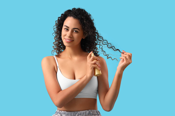 Belle femme afro-américaine pulvérisation de cheveux sur fond bleu - Photo, image