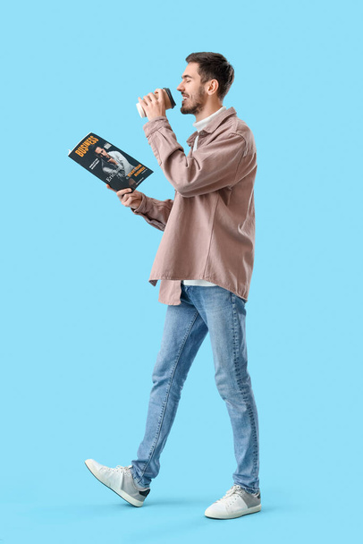 Young man with magazine drinking coffee on blue background - Photo, Image
