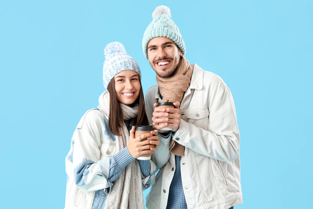 Loving couple in winter clothes with coffee cups on blue background - Photo, Image