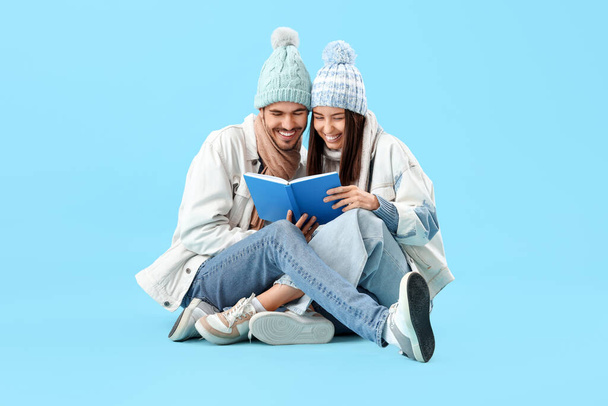 Любляча пара в зимовому одязі читає книгу на синьому фоні - Фото, зображення