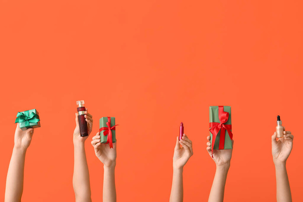 Female hands with different cosmetic products and gifts on orange background - Photo, Image