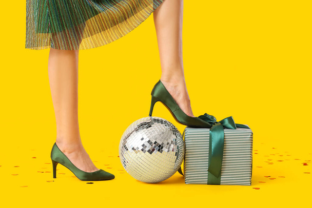 Gyönyörű fiatal nő disco labda és ajándék sárga háttér - Fotó, kép