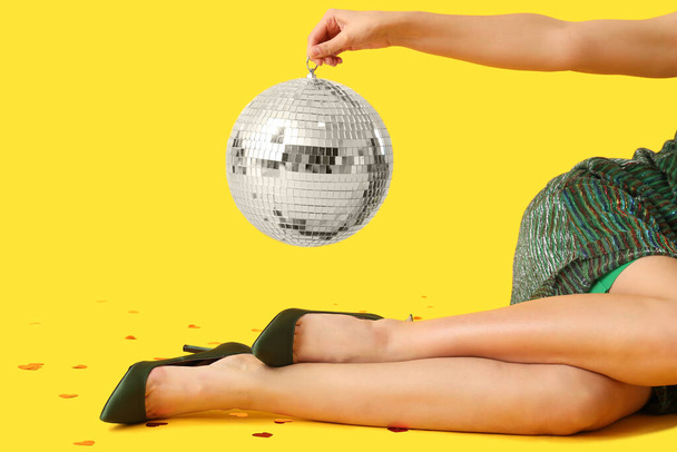 Beautiful young woman with disco ball on yellow background - Photo, Image