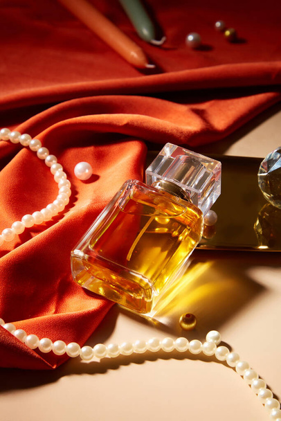 Etiketsiz bir parfüm şişesi bir dizi inci, mum ve kırmızı ipek ile bir masanın üzerinde sergilenir. Boş etiketli parfüm reklamı için bir model. - Fotoğraf, Görsel