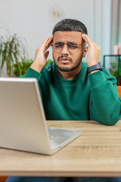 Hombre indio cansado freelancer utilizar el ordenador portátil, que sufre de dolor de cabeza tensión problema, migraña, estrés en el escritorio de la oficina en casa. Guy trabaja en notebook, envía mensajes, hace compras en línea, viendo películas - Foto, imagen