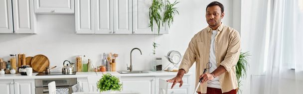 handsome blind indian man in cozy outfit using his walking stick while in his kitchen, banner - Photo, Image