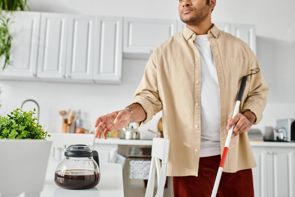 handsome indian man with visual impairment using walking stick and holding coffee while in kitchen - Photo, Image