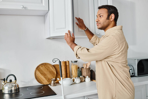 Yakışıklı Hintli engelli adam günlük giysiler içinde bastonla mutfaktaki ürünlere ulaşıyor. - Fotoğraf, Görsel