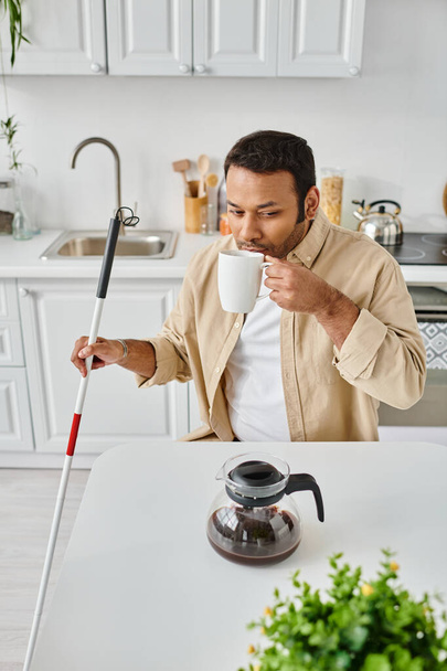 przystojny Indianin człowiek z zaburzenia wzroku siedzi i pije smaczne kawa podczas gdy w kuchni - Zdjęcie, obraz