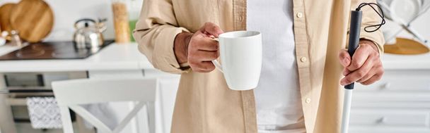 ウォーキングスティックとコーヒーのカップを保持する快適な衣装で盲目であるインド人男性のクロップビュー - 写真・画像