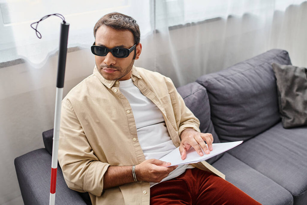 εμφανίσιμος Ινδιάνος με τύφλωση σε γυαλιά που κάθεται στον καναπέ και διαβάζει τον κώδικα Μπράιγ - Φωτογραφία, εικόνα