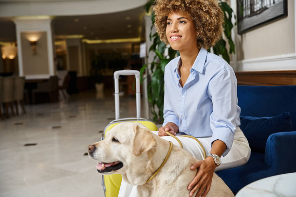 viajero feliz esperando el check-in con Labrador en hotel que acepta mascotas, mujer negra con perro - Foto, Imagen