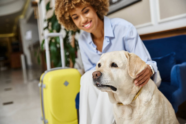 счастливый турист ждет регистрации с лабрадором в дружелюбном к домашним животным отеле, чернокожая женщина с собакой - Фото, изображение