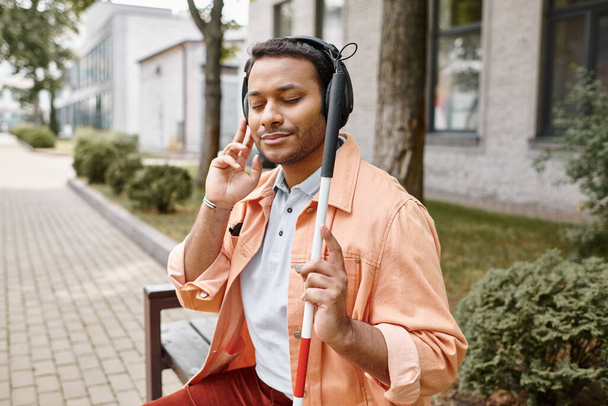 homem indiano alegre com cegueira em fones de ouvido com bengala apreciando música enquanto fora - Foto, Imagem