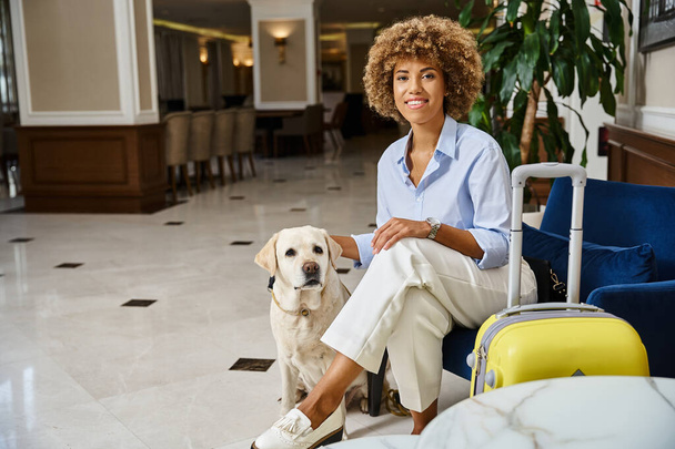 glücklicher Gast wartet mit seinem Labrador im haustierfreundlichen Hotel auf den Check-in, schwarze Frau kuschelt Hund - Foto, Bild