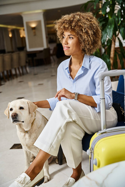 feliz huésped a la espera de check-in con perro en hotel que acepta mascotas, mujer negra con reloj de pulsera moderno - Foto, Imagen