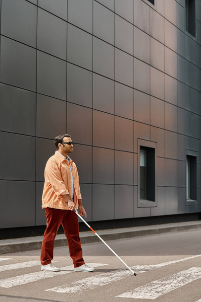 handsome indian disabled man in orange jacket with glasses and stick with gray wall on backdrop - Photo, Image