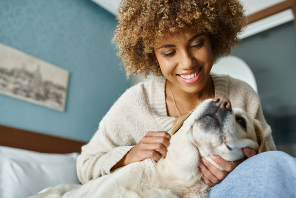 allegro giovane donna afro-americana coccole labrador su un letto in una camera d'albergo pet-friendly - Foto, immagini