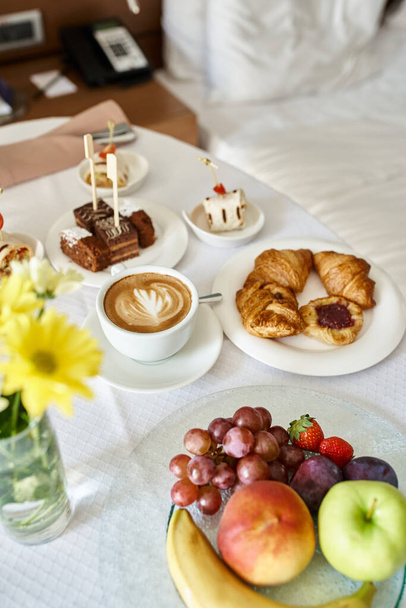 Obsługa pokoju hotelowego ze świeżym cappuccino i różnorodne jedzenie na śniadanie, rogaliki i owoce - Zdjęcie, obraz