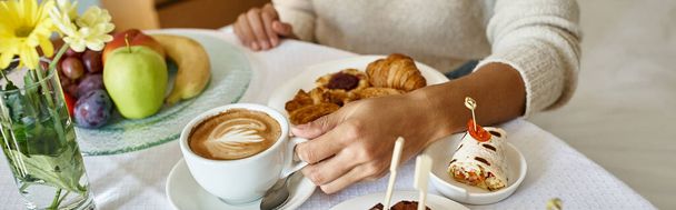 oříznutý prapor africké americké ženy těší cappuccino a pečivo v hotelovém pokoji - Fotografie, Obrázek