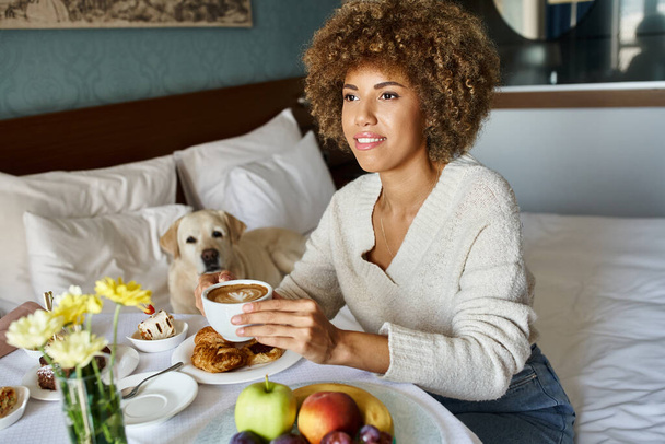 black woman holding cup of cappuccino near labrador dog in pet friendly hotel, room service - Photo, Image