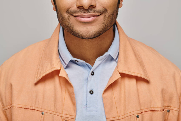 cropped view of cheerful indian man in orange jacket posing on gray backdrop and smiling happily - Photo, Image
