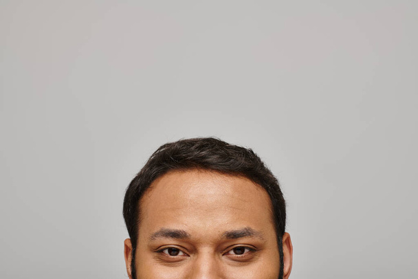 handsome indian male model looking contentedly straight at camera with gray wall on background - Photo, Image