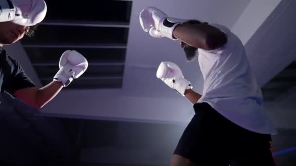 Twee vechters die elkaar confronteren in de boksring... lunchen en slaan. Tegenstrijdende tegenstander in verwarmde Muay Thai trainingswedstrijd met dramatische verlichting - Video