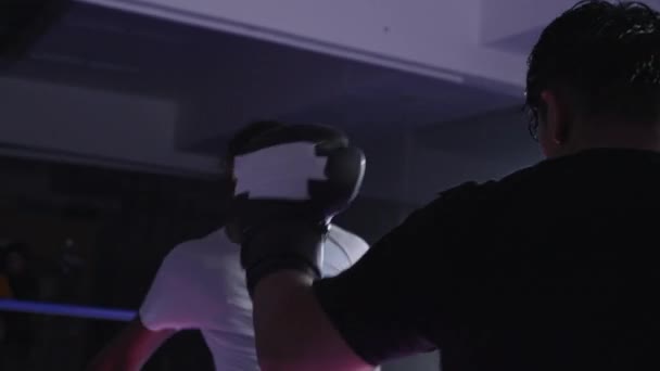 Dos luchadores peleando dentro del ring de boxeo usando guantes. Opositores pateando y golpeándose mutuamente en un enfrentamiento dramático - Metraje, vídeo