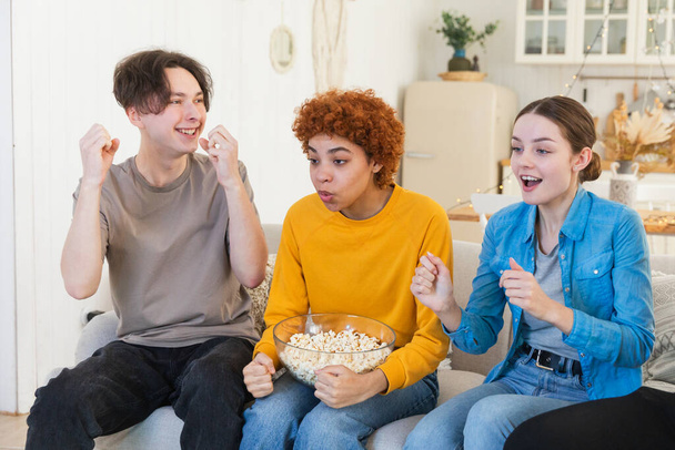Group of friends watching sport match soccer football game on tv. Happy football fans celebrating victory at home. Friendship sports entertainment concept. Diverse buddies having fun together at home - Photo, Image