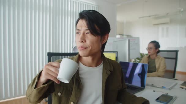 Muotokuva iloinen aasialainen ohjelmoija hymyilee kameralle juodessaan teetä työpaikalla tauon aikana toimistossa - Materiaali, video