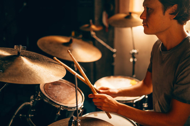 Bubeník hraje na bubny v hudebním studiu na zkoušce kapely. Hudebník s nástrojem v krásném západu slunce z okna. - Fotografie, Obrázek