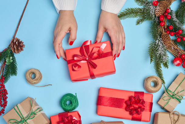 Nainen pakkaa lahjoja, ennen joulua vilskettä ja valmistautuu jouluun. Lahjat kääritty punaiseen paperiin ja sidottu nauhalla   - Valokuva, kuva