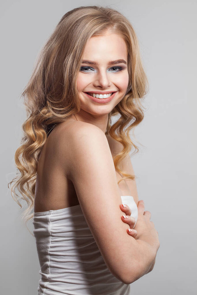 Vrolijk jong vrouwelijk modelportret. Blond vrouwtje met lang golvend haar, make-up en schone huid op witte achtergrond - Foto, afbeelding