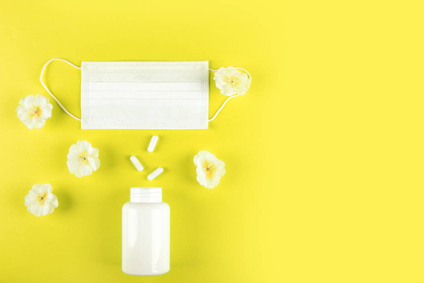 Білі квіти на жовтому тлі поєднуються з медичною маскою і контейнером таблеток для капсул, підкреслюючи важливість включення як природних, так і медичних підходів до здоров'я. - Фото, зображення