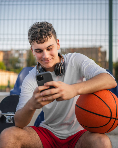 Kaukasischer Teenager benutzt Handy-Smartphone auf Basketballplatz - Foto, Bild