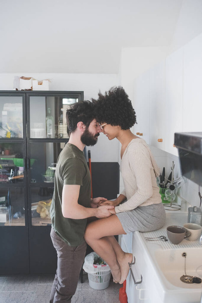 Jeune couple multiethnique posant souriant embrassant ensemble à la maison - Photo, image