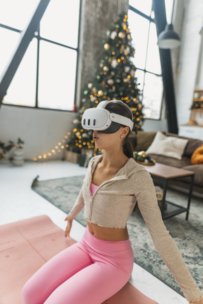 Utilizando un auricular de realidad virtual, el entrenador de yoga lleva a cabo sesiones en línea en medio de las vacaciones de Año Nuevo. Foto de alta calidad - Foto, Imagen