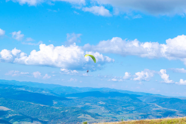 Αλεξίπτωτο με εκπαιδευτή. Σιλουέτα του paraglider με φόντο ένα όμορφο τοπίο του μπλε συννεφιασμένο ουρανό και πράσινα βουνά. Πάνω θέα από το βουνό. Ακραίο χόμπι και περιπέτεια. - Φωτογραφία, εικόνα