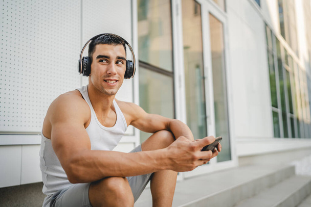 Портрет молодого человека под открытым небом использовать наушники и смартфон, чтобы играть в видеоигры - Фото, изображение