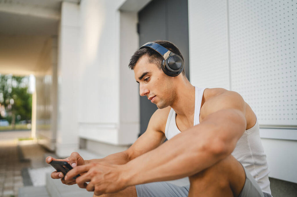 Porträt eines jungen Mannes, der im Freien mit Kopfhörern und Smartphone Videospiele spielt - Foto, Bild