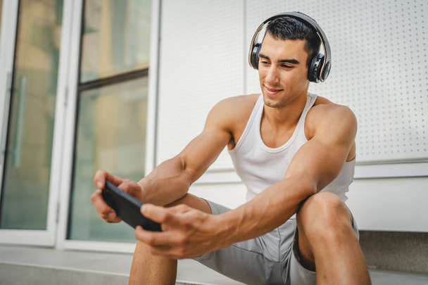 Portré fiatal férfi kültéri használatra fejhallgató és okostelefon játszani videojátékok - Fotó, kép