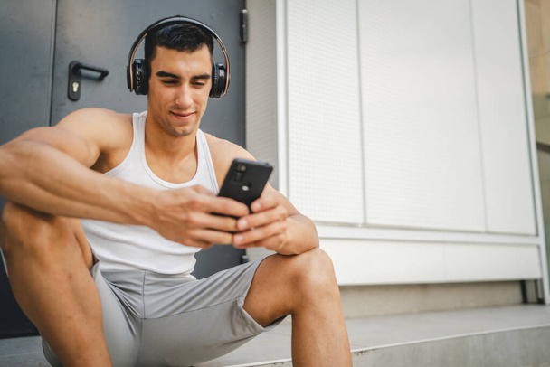 Portret młodego mężczyzny na zewnątrz za pomocą słuchawek i smartfona do odtwarzania muzyki lub oglądania podcastu wideo - Zdjęcie, obraz