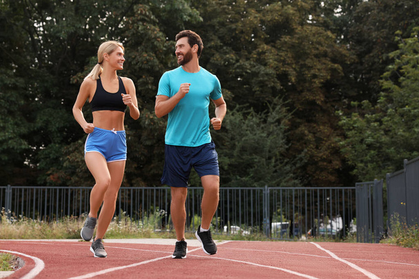 Healthy lifestyle. Happy sporty couple running at stadium, space for text - Φωτογραφία, εικόνα